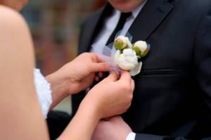 Who attaches the boutonniere and how?