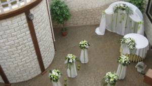 Low columns with white flowers and green leaves in front of the arched entrance to the banquet hall