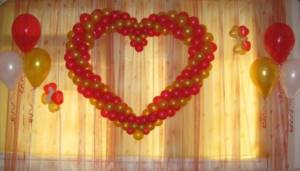 Ровное красно-золотистое сердце из воздушных шариков на шторе