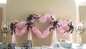 Heart-shaped decoration made of green flowers and small white and pink balloons